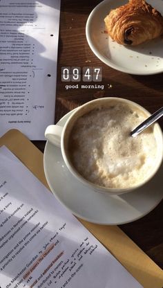 there is a cup of coffee and croissant on the table next to an open book