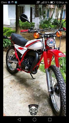 a red and white dirt bike parked on the side of a road in front of a house