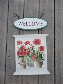 a welcome sign hanging from the side of a wooden wall with potted flowers on it