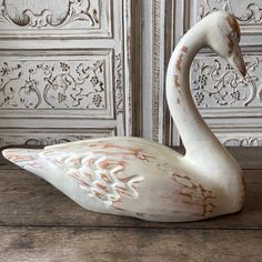 a white swan statue sitting on top of a wooden table next to a wall with ornate carvings