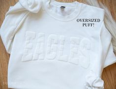 Personalized OVERSIZED Puff Print Team Sweatshirt Team Name Sweatshirt Christmas Gift for Mom Sons Jersey Number Football Baseball Sports Sweatshirt Custom Embossed Puff Christmas Gift for Him School Spirit Sweatshirt The main listing image (EAGLES) is white sweatshirt, white puff text PLEASE RECORD YOUR TEXT IN ALL CAPITAL LETTERS THIS IS ONE LINE OF TEXT ONLY - ARCHED LIKE OUR PHOTO, IN PUFF PRINT - EITHER WHITE, OR BLACK - NO OTHER COLORS AVAILABLE. Template size is 12" - THIS LISTING ONLY Monochromatic tones : white/white, black/black Please note - the puff does have texture. Its not entirely smooth - THIS IS NORMAL    DETAILS    Our Personalized Team Name Sweatshirt boasts an exceptional level of softness and comfort - SO COZY! Designed as unisex apparel, we recommend reviewing our si Puff Letter Sweatshirt, White School Spirit T-shirt For Winter, White School Spirit Tops With Letter Embroidery, White Tops With Letter Embroidery For School Spirit, Team Sweatshirts, Sports Sweatshirt, Photo Care, Name Christmas, Christmas Gift For Mom