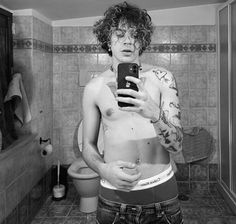 a man in the bathroom taking a selfie with his cell phone and tattoos on