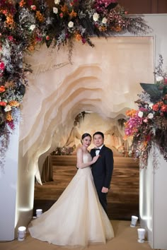 a newly married couple posing for a photo in front of an archway decorated with flowers