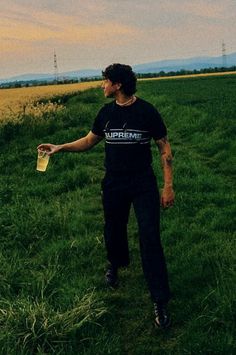 a man standing on top of a lush green field next to a tall grass covered hillside