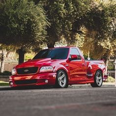 a red pick up truck parked on the side of the road in front of some trees