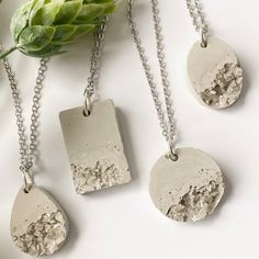 three pendants are shown on a white surface next to a green plant and some leaves