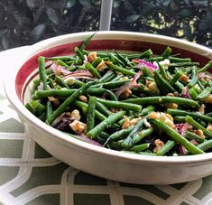 a bowl filled with green beans, onions and walnuts on top of a table