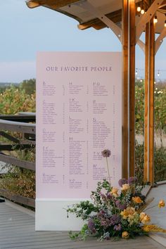 a seating chart on a wooden structure with flowers in the foreground and lights above it