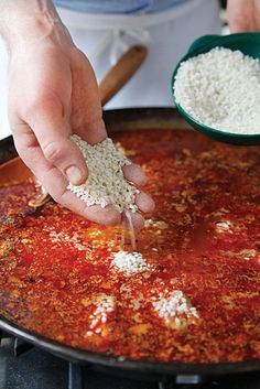 a person scooping rice into a skillet on top of a stove with other cooking utensils