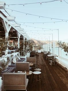 an outdoor seating area with tables and chairs on a wooden deck next to the ocean