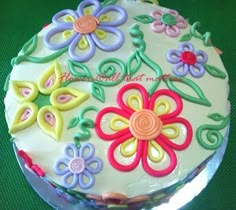 a cake decorated with colorful flowers and swirls on a green tableclothed surface