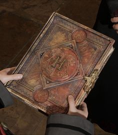 two hands holding an old book in front of the camera, while another person looks down at it