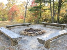 a fire pit surrounded by wooden benches in the woods