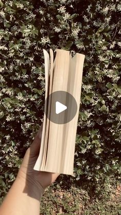 someone is holding up an open book in front of some bushes and trees with the words,