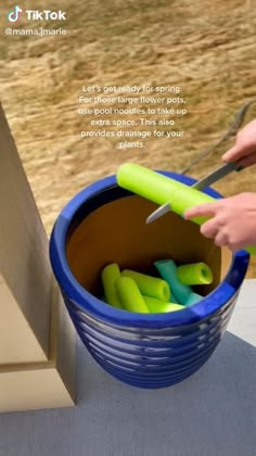 a person is cutting something in a blue bucket with green handles and plastic tongs