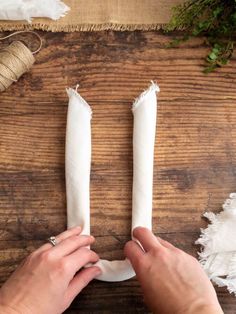 two white candles are being held by someone's hands on a wooden table with other items