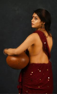 a woman in a red sari holding a brown object with gold dots on it