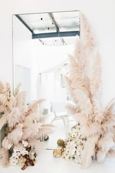 a mirror and some flowers on the floor in front of a white wall with mirrors