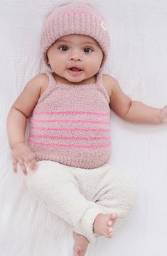 a baby wearing a pink and white striped top laying on a bed with her hands out