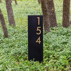 a black sign sitting in the grass near some trees