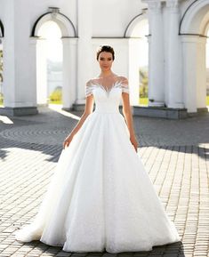 a woman in a white wedding dress standing on a cobblestone walkway with arches