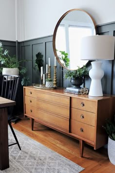 a living room with a dresser, mirror and plants on the sideboard in front of it