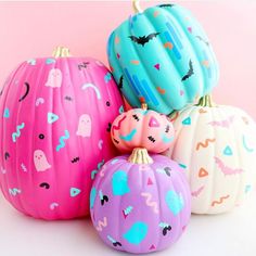 four painted pumpkins sitting next to each other on a white surface with pink and blue background