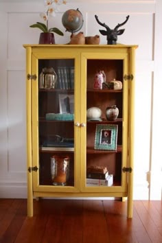 a yellow cabinet with books and vases on top