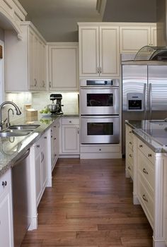 a kitchen with white cabinets and stainless steel appliances, wood flooring and hardwood floors