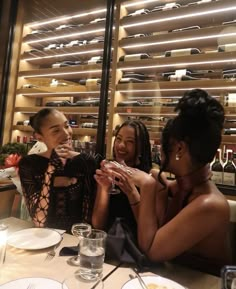 three women sitting at a table with wine glasses in their hands and plates on the table