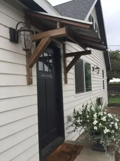 a white house with a black door and some flowers on the front porch, next to it is a potted plant