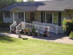 a house with white railings and flower pots on the front porch, next to a lawn