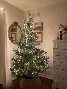 a small christmas tree in a basket on the floor next to a dresser and mirror