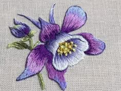 a purple flower with green leaves is embroidered onto a piece of fabric on a table cloth