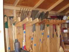 there are many tools hanging on the wall in this room, including shovels and rakes