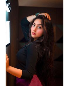 a woman with long hair is leaning against a wall and looking at the camera while wearing a black top