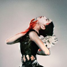 a woman with red hair and black dress holding her arms behind her head while standing in front of a gray background