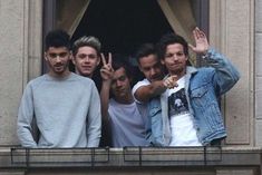 four young men are standing on the balcony and making peace signs with their hands in front of them