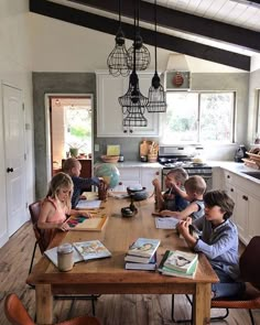 a group of children sitting at a table with books on it in a kitchen area