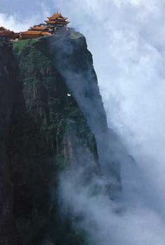 a tall mountain with some buildings on it's side in the clouds and fog