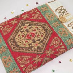 a red, green and beige rug with buttons on the bottom is laying on a white surface