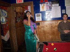 a woman in a green sequin dress singing into a microphone next to a pool table