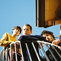 four men standing on the balcony of a building with their arms around each other looking at something