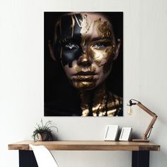 a woman's face is covered in gold and black paint, as she sits on a desk