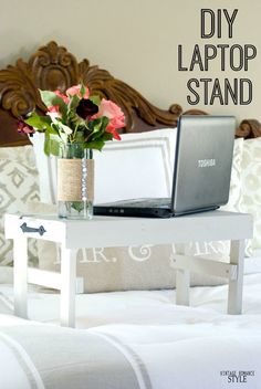 a laptop computer sitting on top of a white table next to a vase with flowers