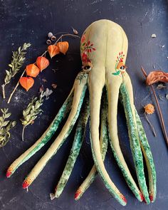 an octopus stuffed animal sitting on top of a table next to dried flowers and leaves