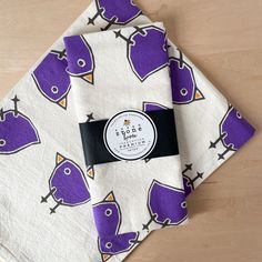 two napkins with purple birds on them sitting on top of a wooden table next to each other