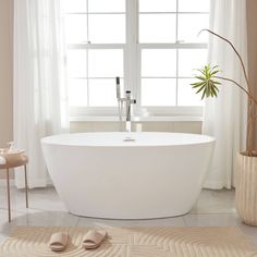 a white bathtub sitting next to a window in a bathroom with beige rugs