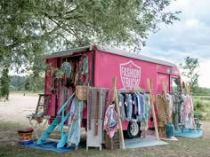 a pink truck parked under a tree with clothes hanging from it's racks and umbrellas