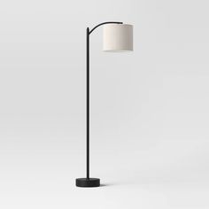 a black floor lamp with a white shade on the base and a round light fixture